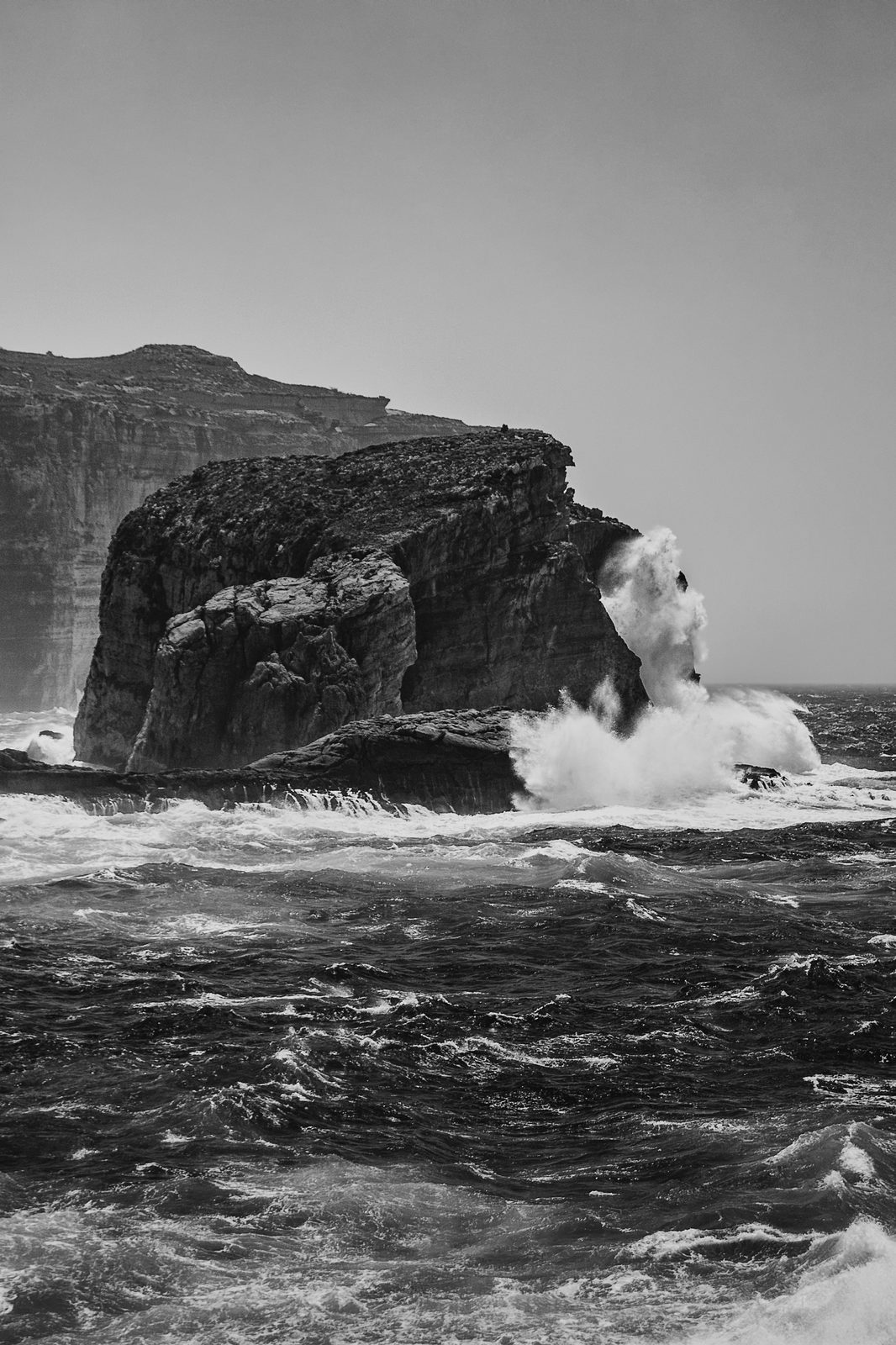 A wave bursting against Ġebla tal-Ġeneral rock in black and white, Dwejra, Gozo